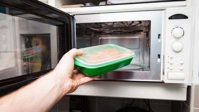 A hand putting a green plastic food container into a microwave